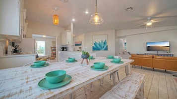 A modern kitchen with a white and blue color scheme, a large island with teal bowls, and a TV mounted on the wall.