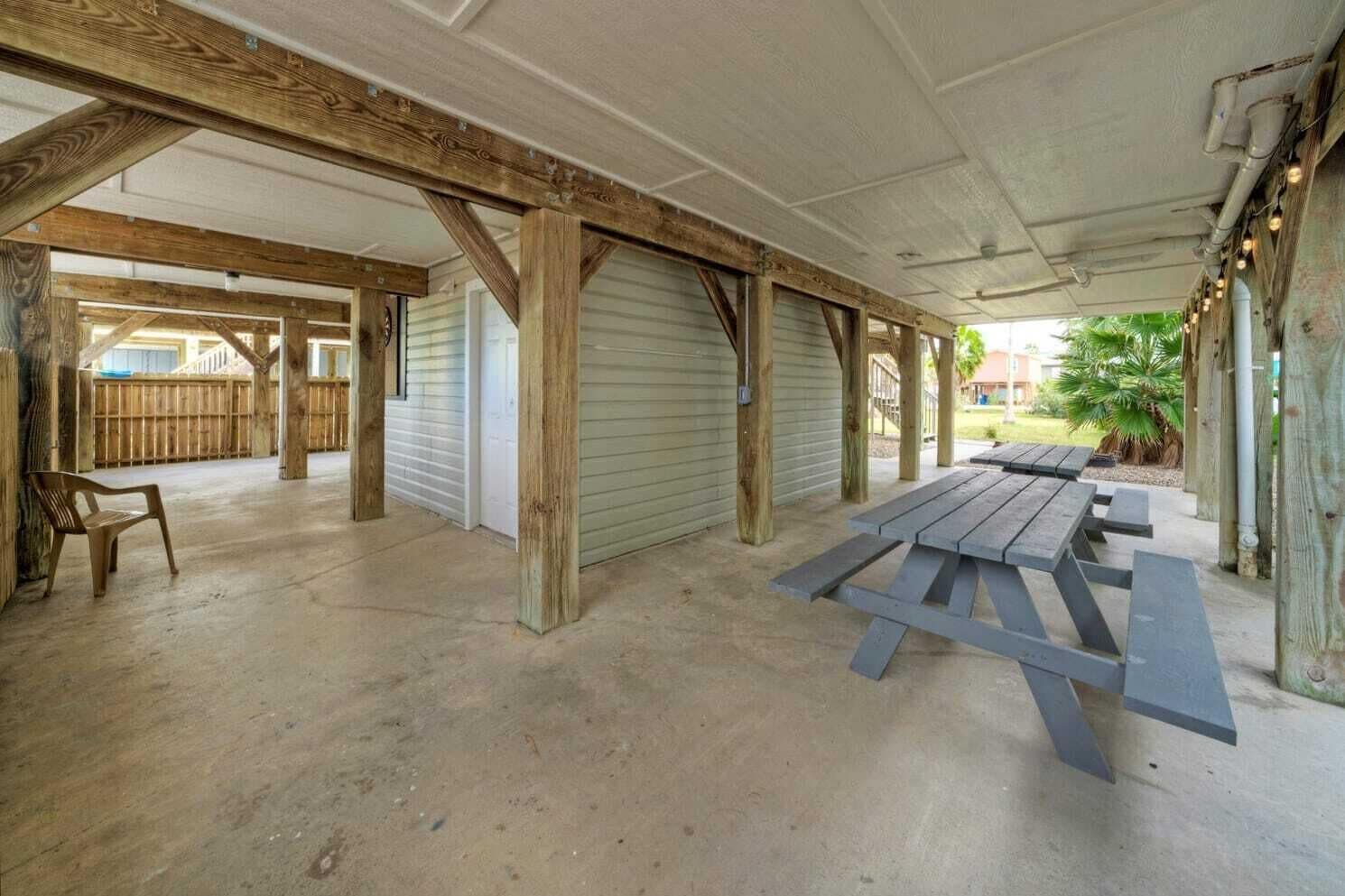 Un espace extérieur couvert, avec des poutres en bois, un sol en béton et une table de pique-nique.