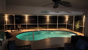 A swimming pool with a ceiling fan, surrounded by wicker furniture and a sign that reads 'Life is better by the pool.'