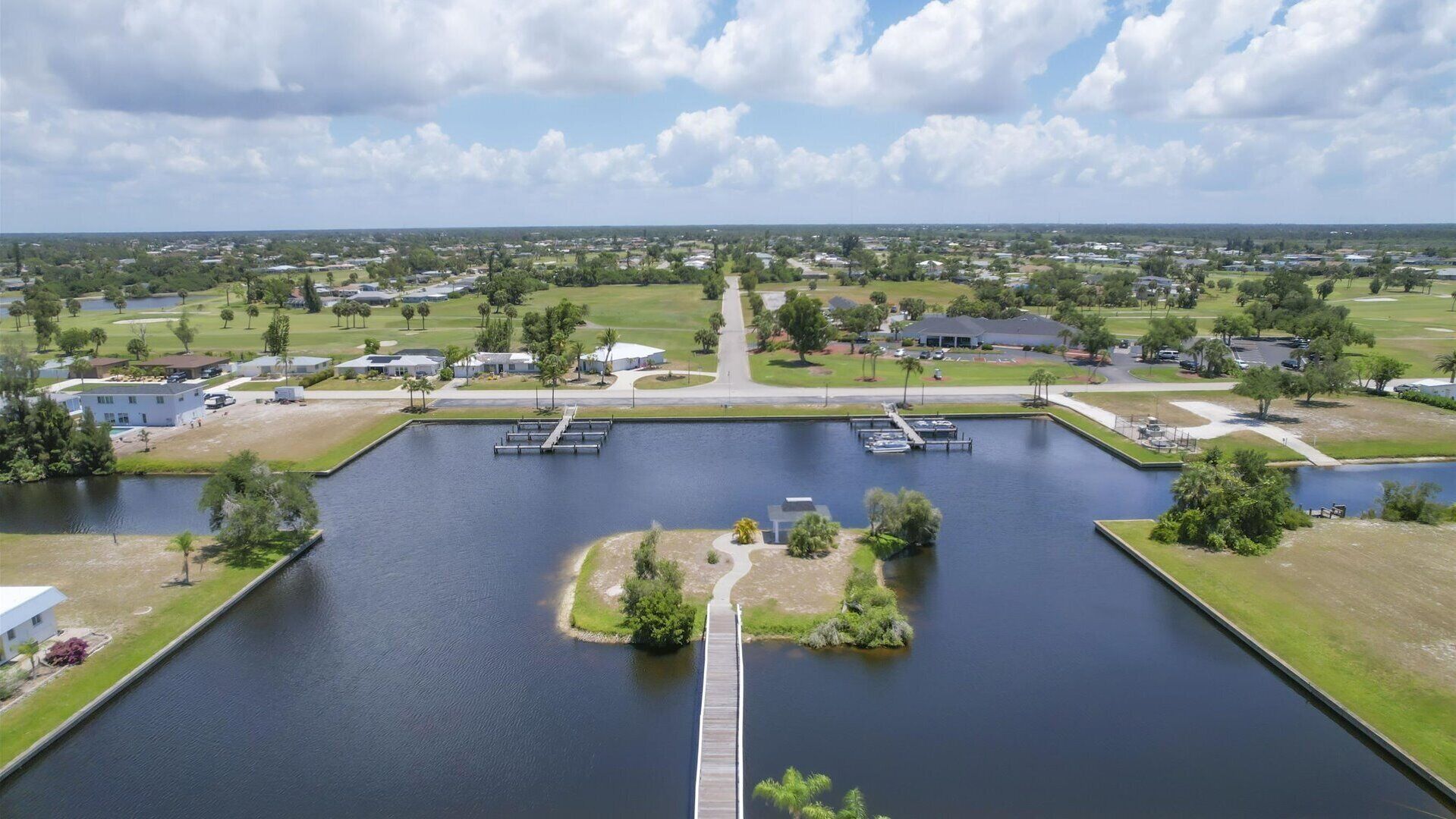 A large body of water with a dock, surrounded by greenery and residential buildings.