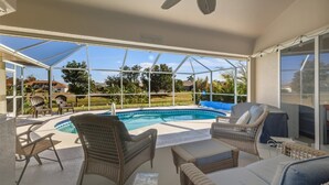 A covered outdoor area with a pool, wicker furniture, and a view of the surrounding landscape.
