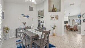 A spacious dining area with a large table and chairs, a kitchen in the background, and a view of the living area.
