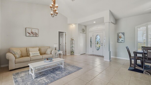 A spacious living room with a striped sofa, a white coffee table, and a chandelier. There is a dining area with a table and chairs.