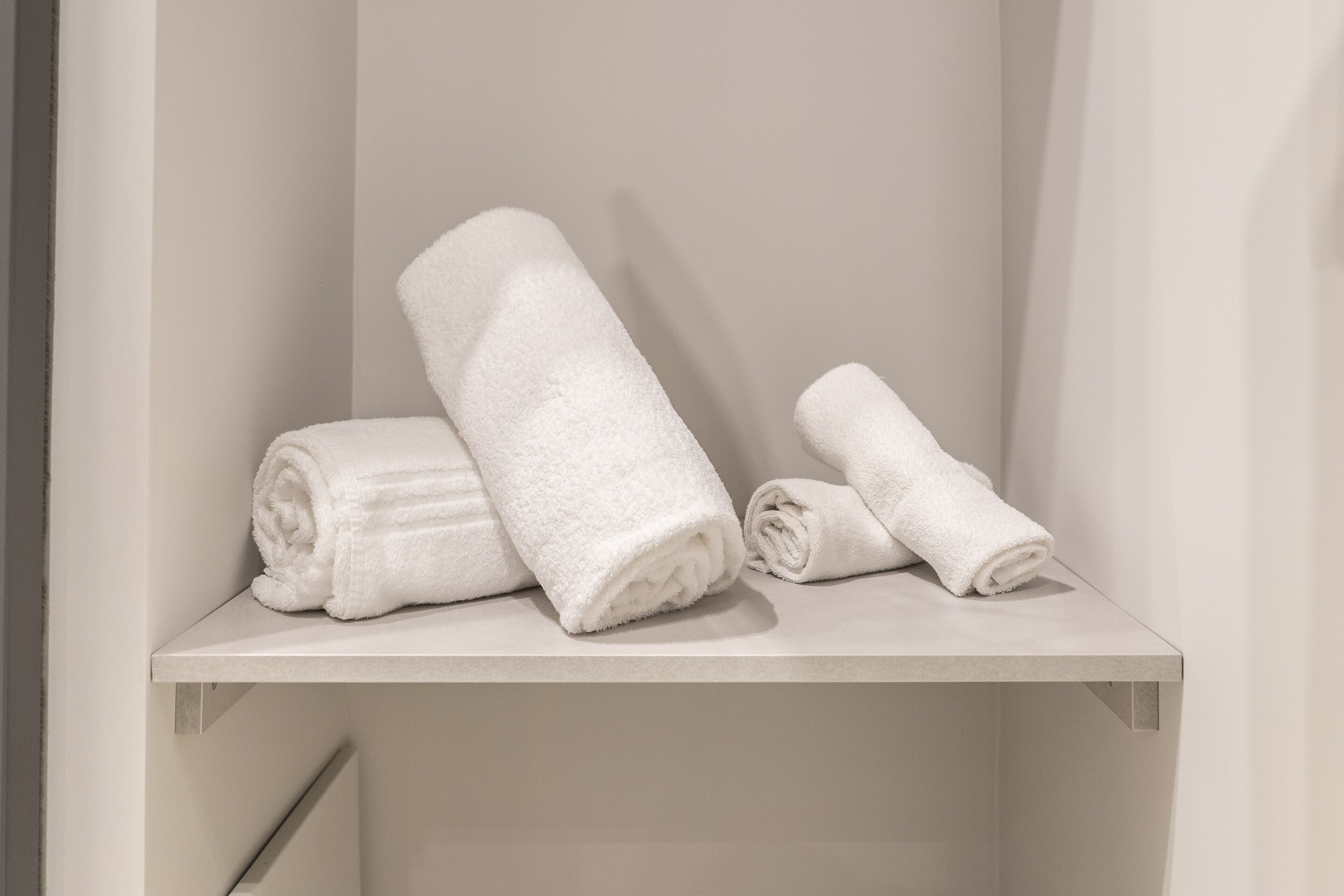 A bathroom with a white towel rack holding three neatly folded towels.