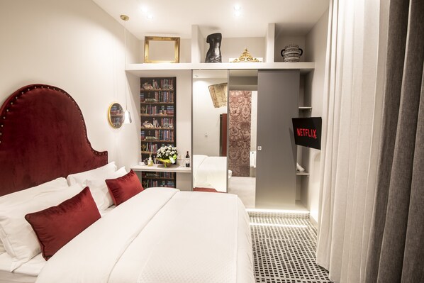 A hotel room with a large bed, a bookshelf, a TV, and a bathroom visible through an open door.