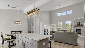 A spacious kitchen with a central island, a dining area with a table and chairs, a gray sofa, and a fireplace.