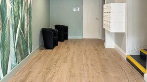 A room with a wooden floor, a wall with a large plant mural, black trash bins, and a white cabinet with drawers. - O'Bistrot Saint-Jacques (Saint-Flour)