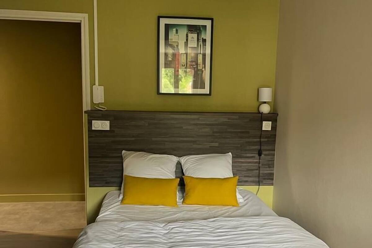 A neatly made bed with white and yellow bedding, a dark headboard, and a framed picture on the wall.