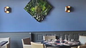 A restaurant interior with a round table set for dining, cushioned chairs, and a decorative wall piece. - O'Bistrot Saint-Jacques (Saint-Flour)