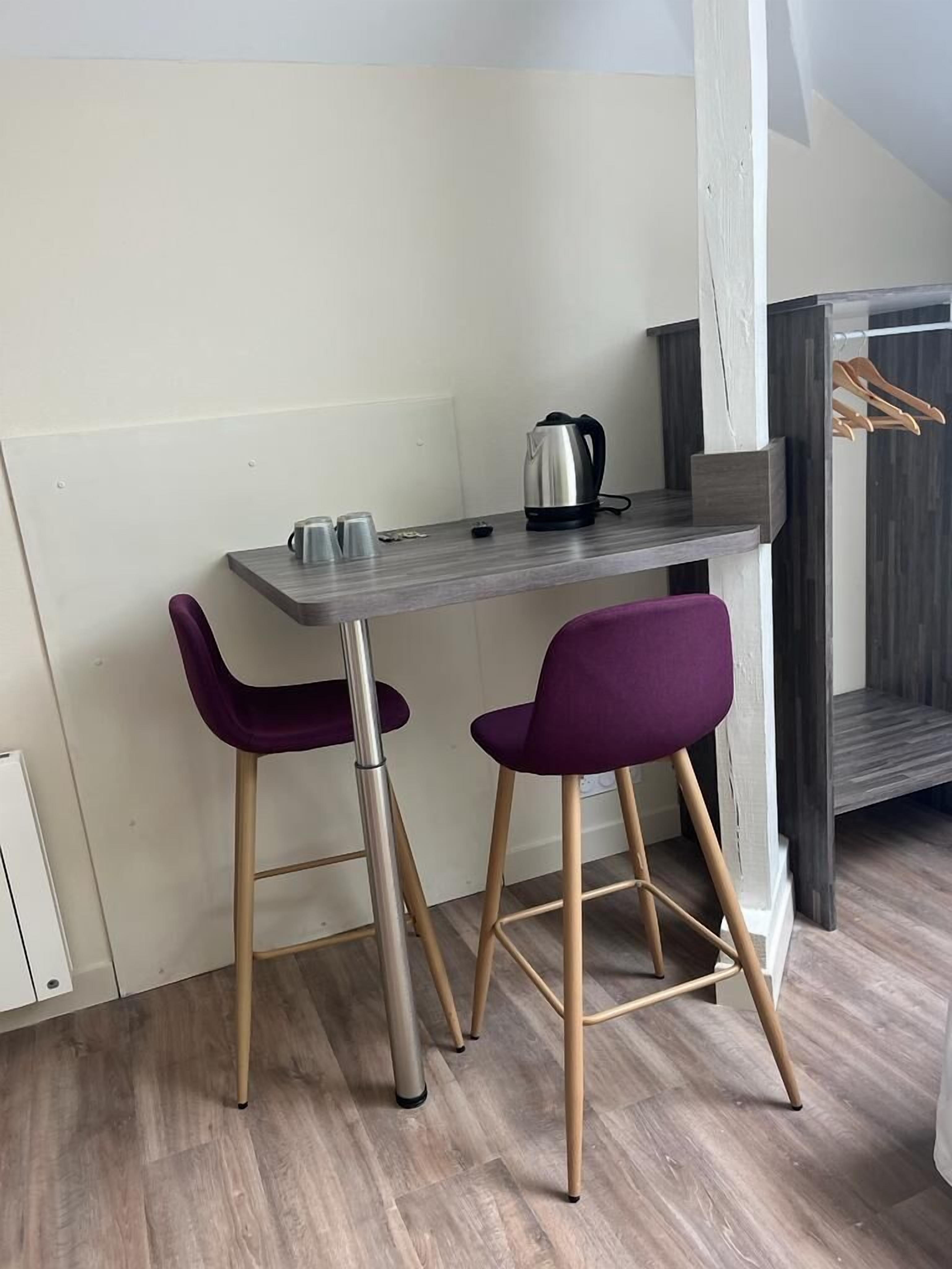 A small kitchenette with a grey countertop, two purple bar stools, and a kettle.