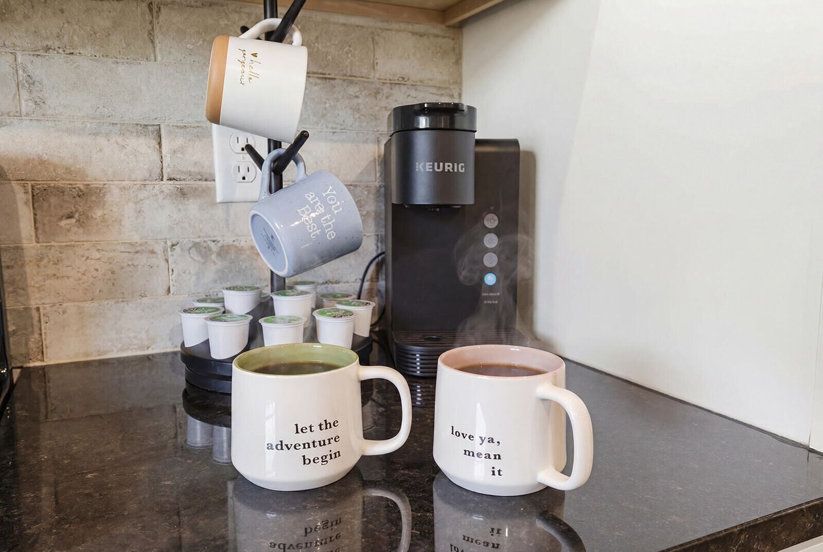 A coffee machine, two mugs with motivational phrases, and a mug pouring coffee into a cup.