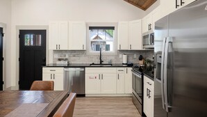 Una cocina moderna con armarios blancos, electrodomésticos de acero inoxidable, techo de madera y ventana con vista a una casa.