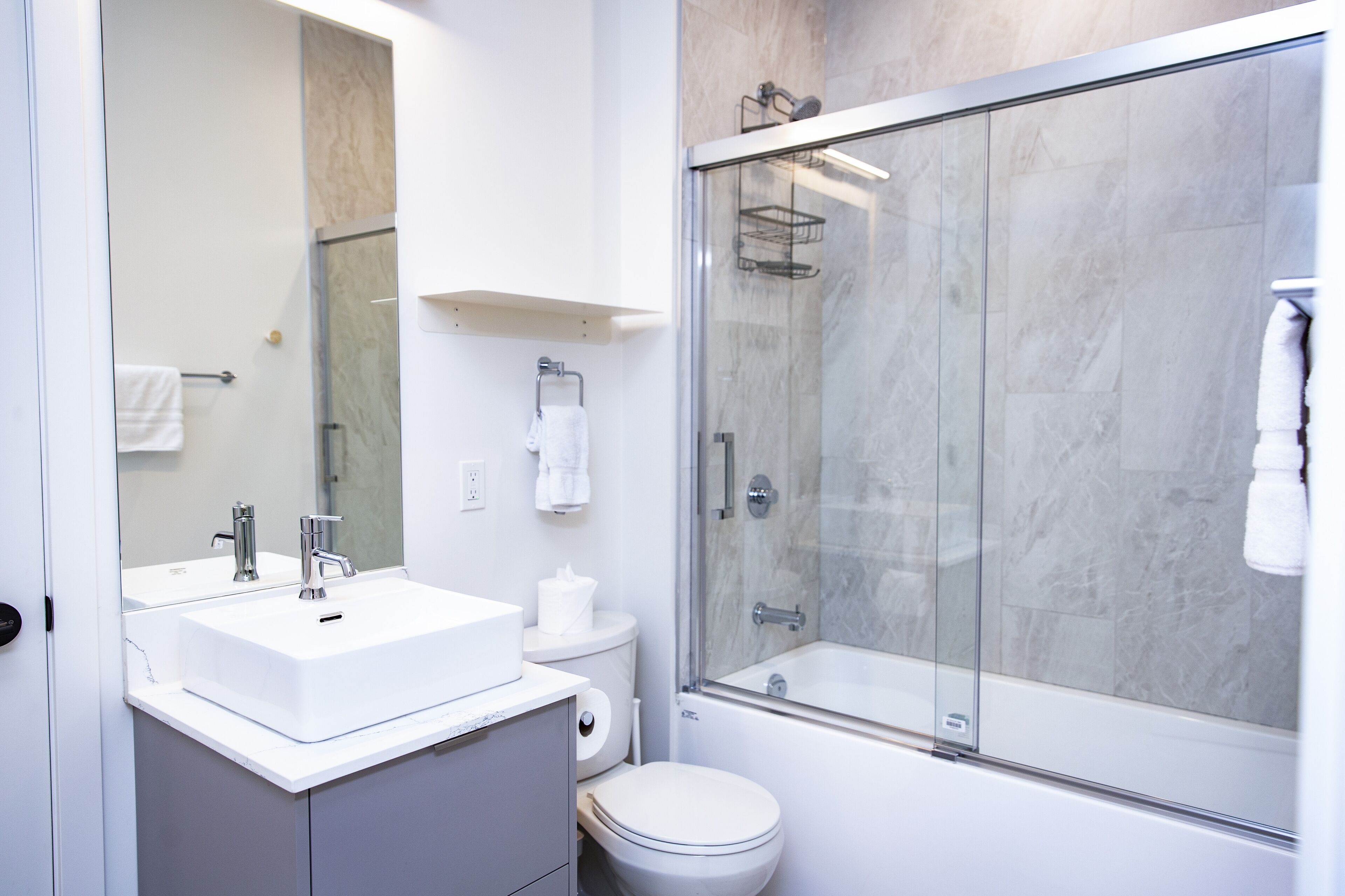 A modern bathroom with a white sink, mirror, and glass-enclosed shower.
