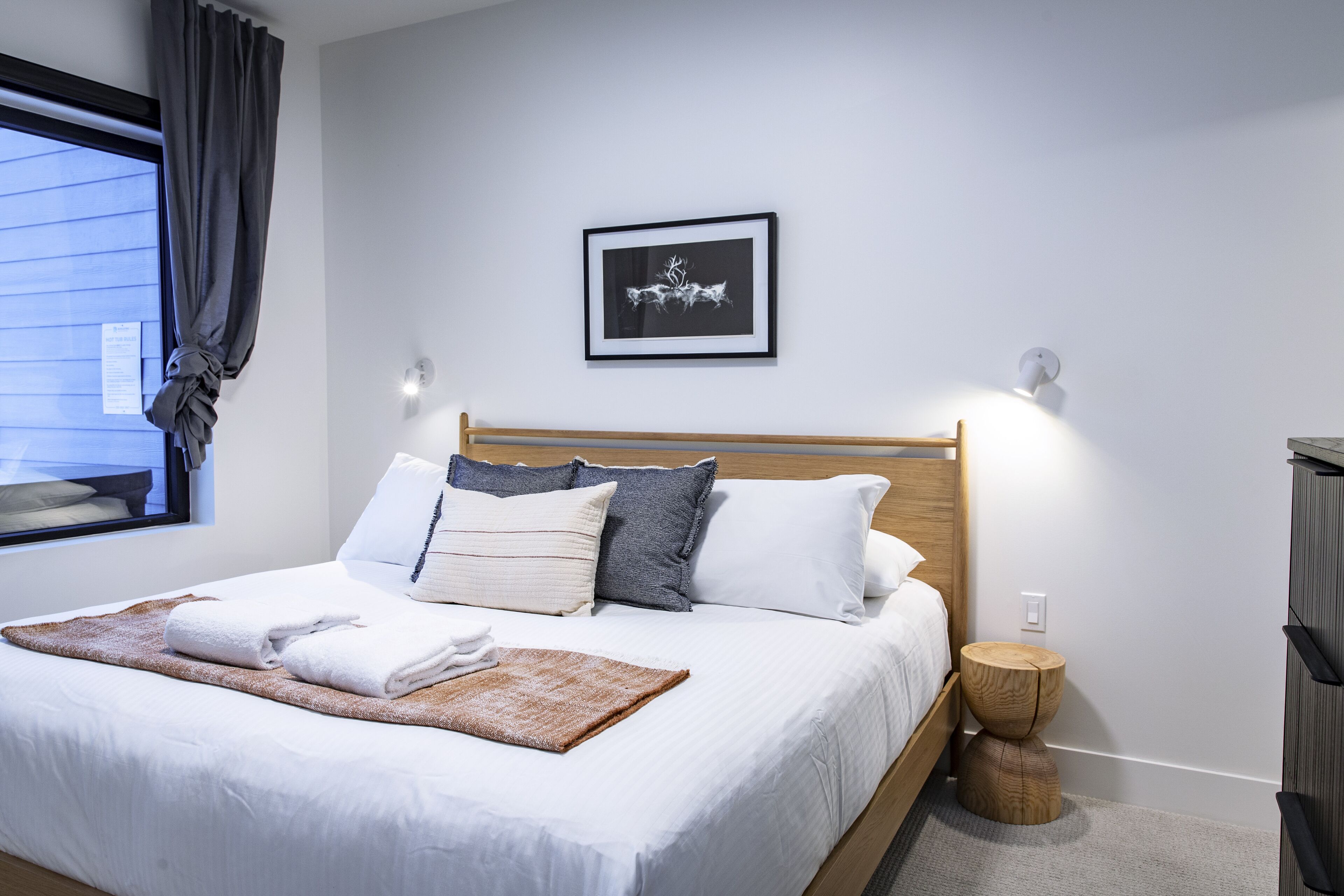 Een netjes opgemaakt bed met witte lakens, een bruine plaid en een lijst met een foto erboven.
