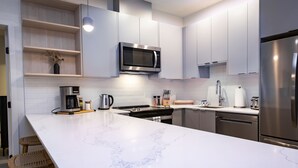 Une cuisine moderne avec des plans de travail en marbre blanc, des appareils électroménagers en acier inoxydable et des étagères en bois.