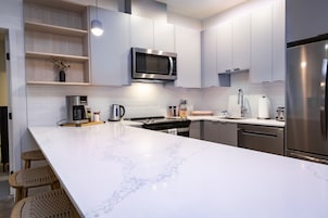 Una cocina moderna con encimeras de mármol blanco, electrodomésticos de acero inoxidable y estantes de madera.