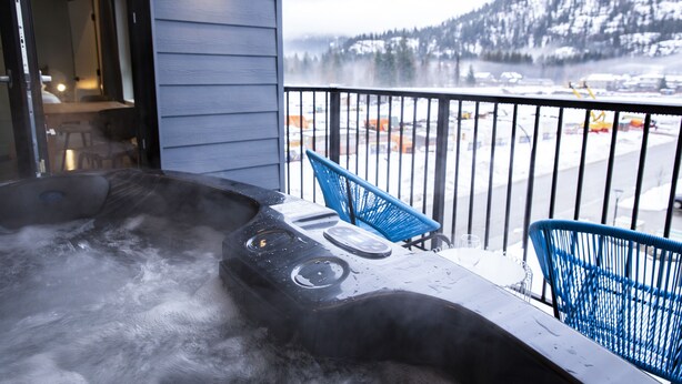 Un bain à remous sur un balcon offrant une vue sur un paysage enneigé et des montagnes.