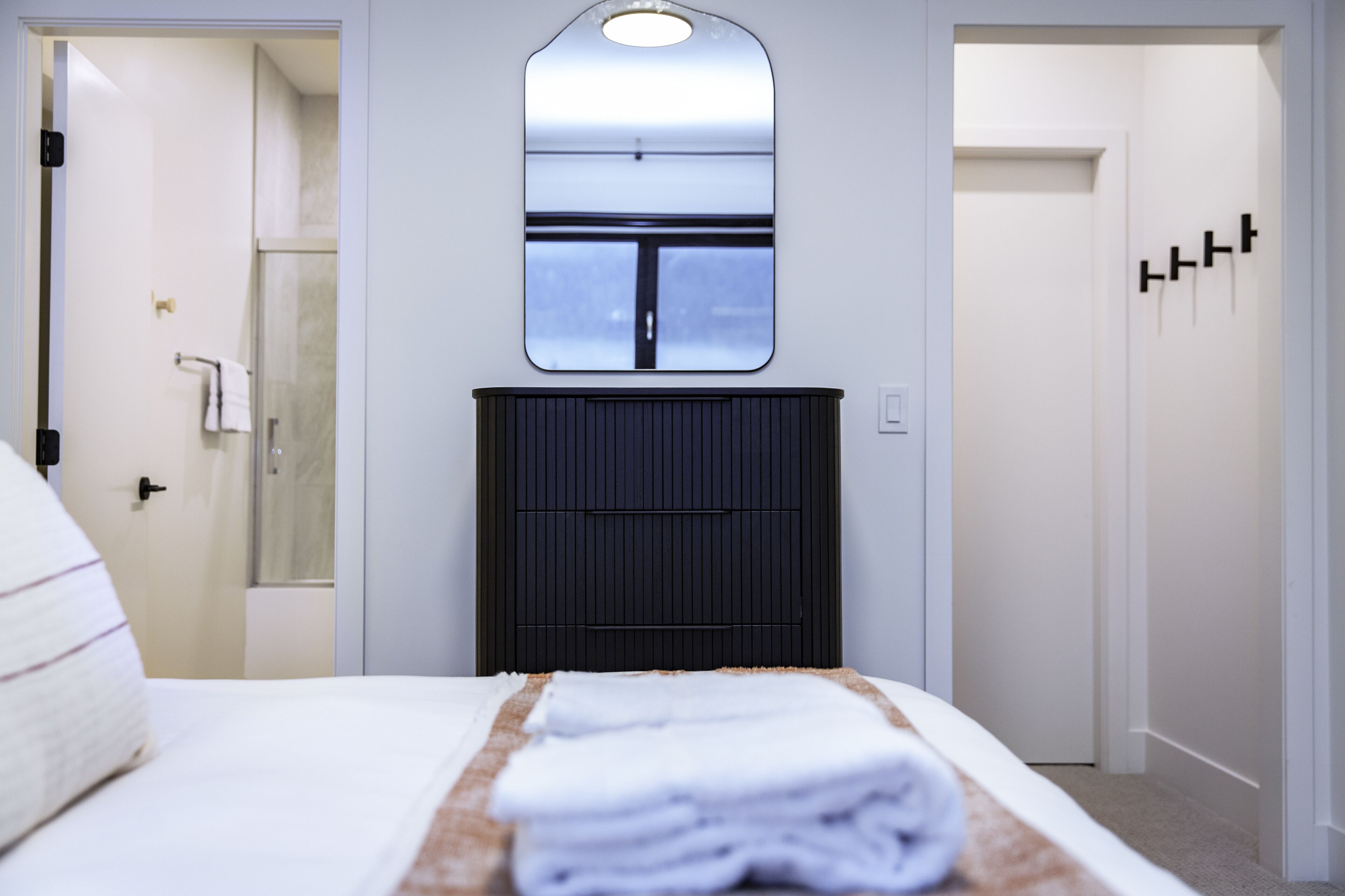 A hotel room with a bed, a black headboard, a mirror, and a door leading to a shower.