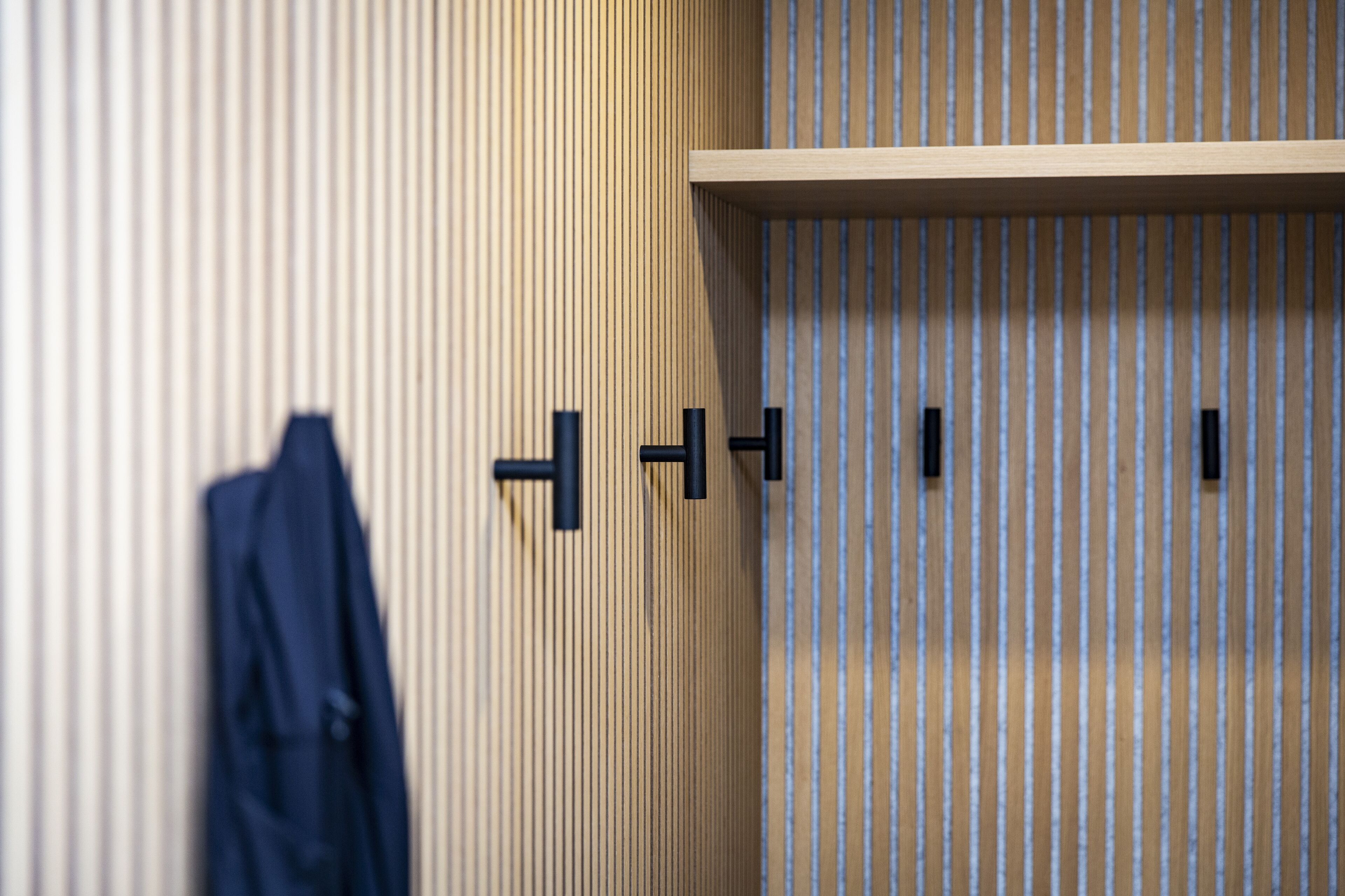 A room with a striped wall, a wooden shelf, and a hanging coat.