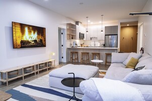 Una sala de estar moderna con chimenea, un sofá, una mesita redonda y una zona de cocina con taburetes de bar.