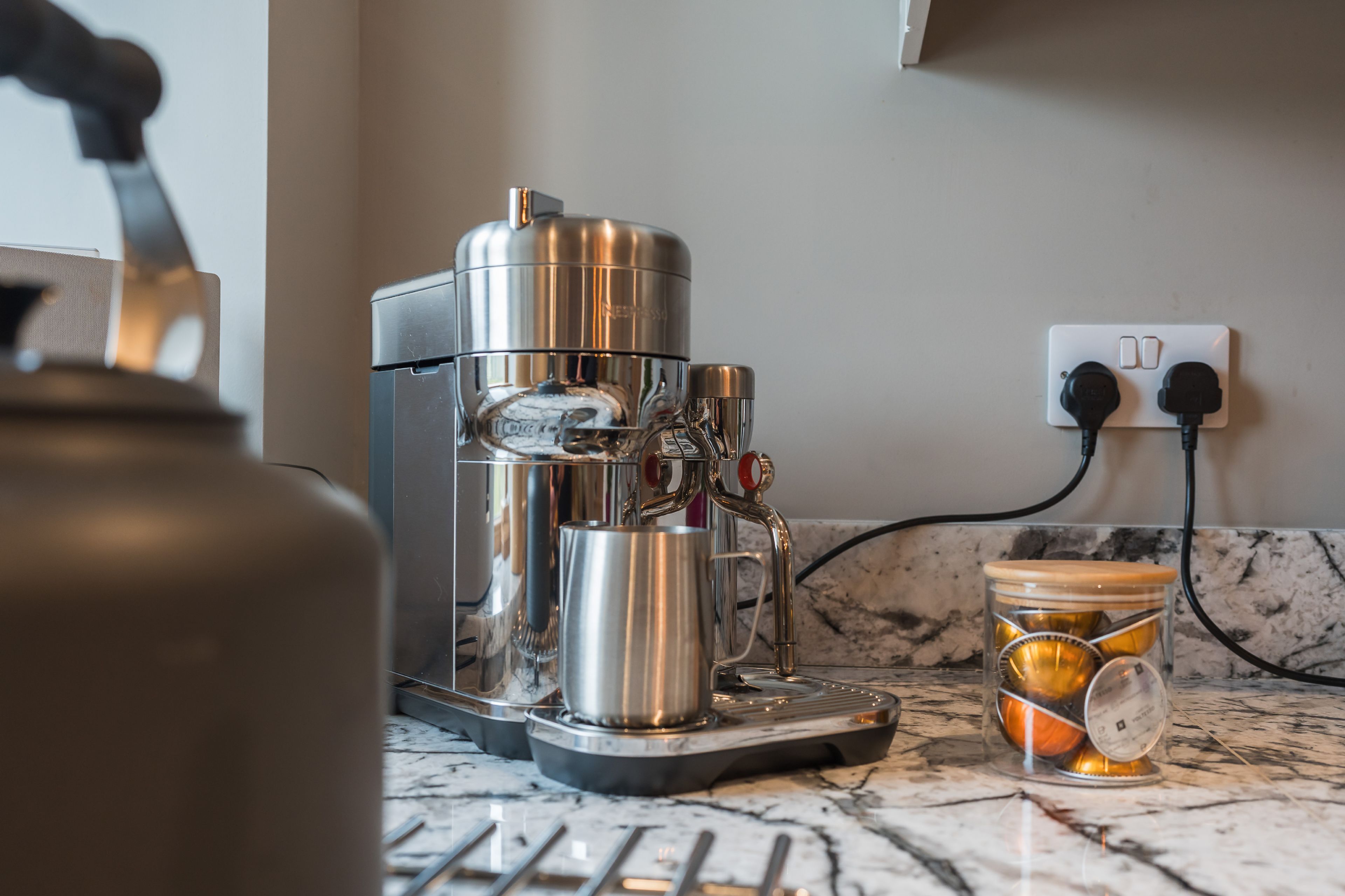A coffee machine on a marble countertop with a glass jar containing coffee capsules.