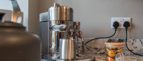 A coffee machine on a marble countertop with a glass jar containing coffee capsules.
