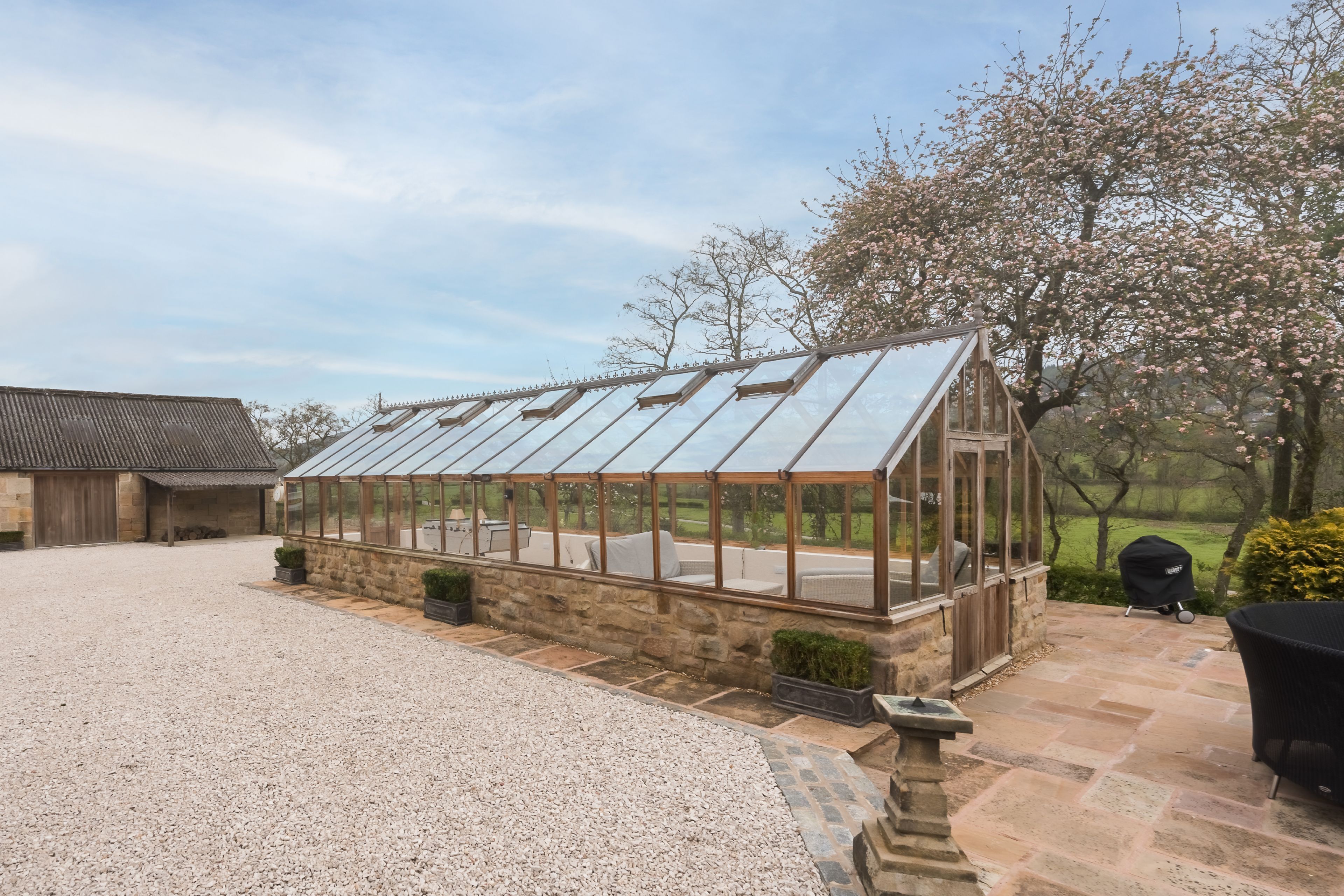 A greenhouse with a glass roof, stone walls, and a gravel driveway.