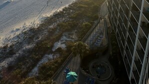 Une vue sur la plage depuis un immeuble de grande hauteur, avec un ciel dégagé et le soleil se couchant sur l’océan.