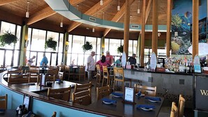 Un restaurant spacieux avec de hauts plafonds en bois, de grandes fenêtres et un coin bar.