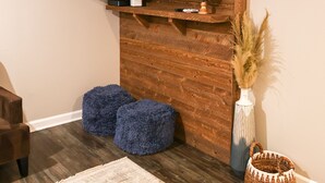 Een woonkamer met een wandgemonteerde flatscreen televisie, houten lambrisering, een wereldbol, blauwe poufs, een vaas met gedroogde planten en een geweven mand.