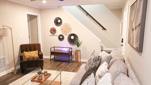Een woonkamer met een bruine leren fauteuil, een grijze bank, een salontafel en een klein bijzettafeltje met een plant.