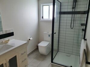 Ein Badezimmer mit Toilette, einer Duschkabine, einem Waschbecken und einem Fenster.
