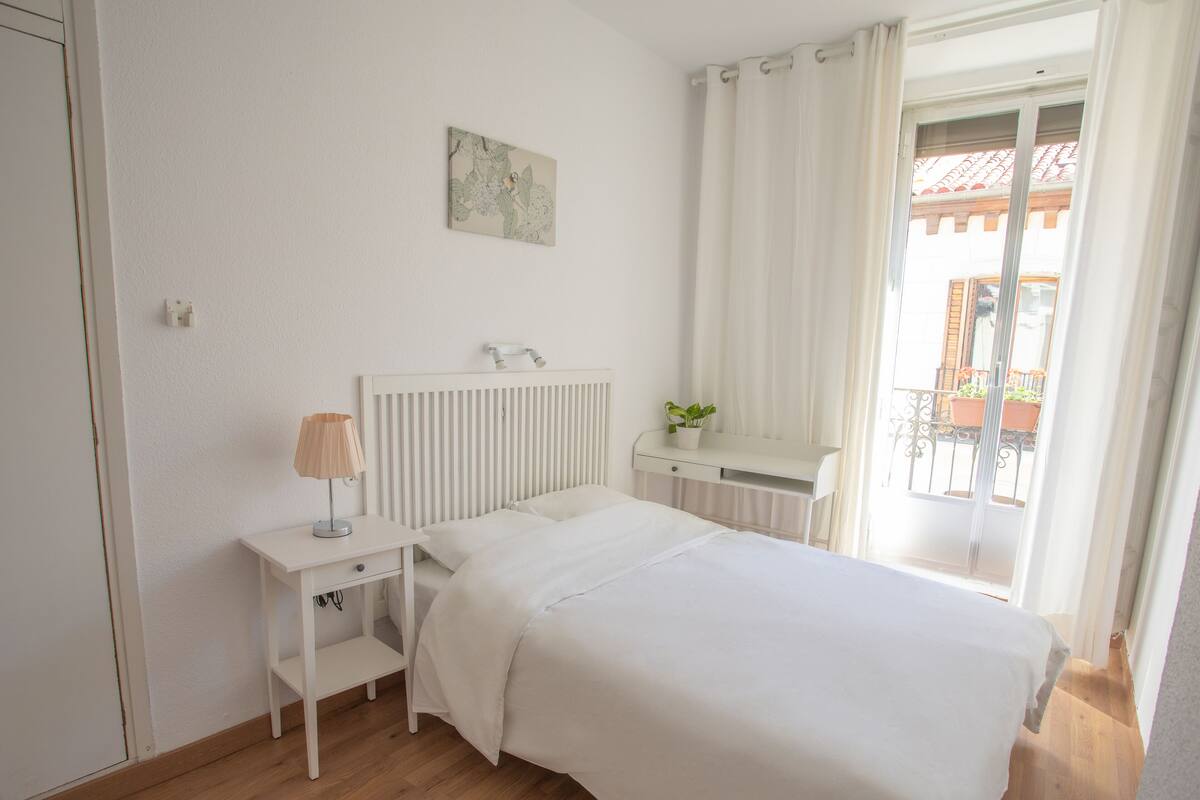 Une chambre à coucher avec un lit, une table de chevet, une lampe et une fenêtre avec des rideaux.