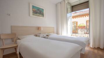 A hotel room with two beds, a wooden headboard, a nightstand, a chair, and a window with curtains.
