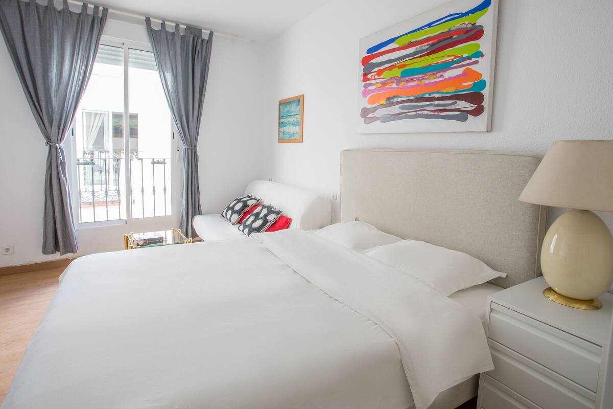 Une chambre d’hôtel avec un lit, une table de chevet, une lampe, un tableau et une fenêtre avec des rideaux.