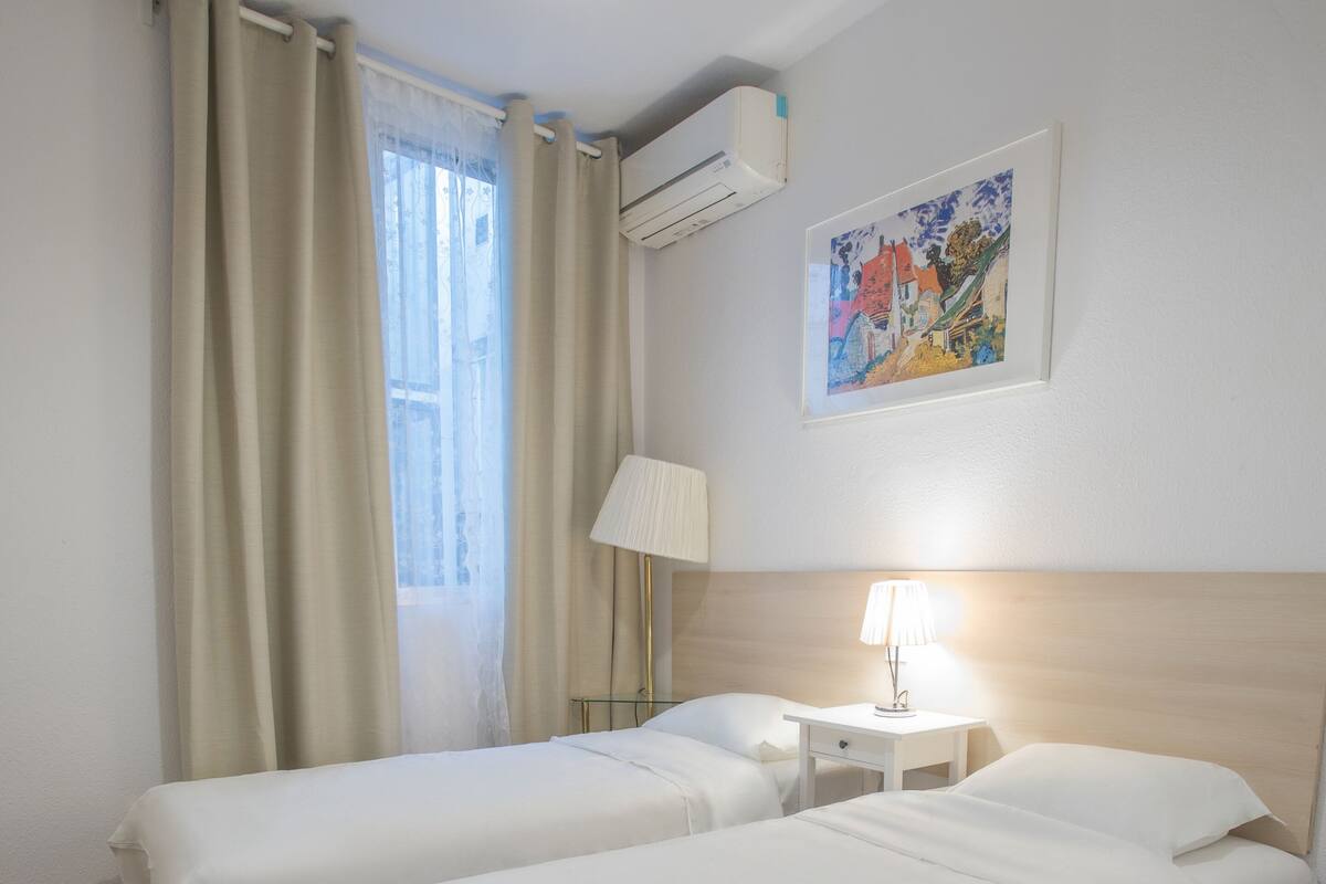 Une chambre d’hôtel avec deux lits, une table de chevet avec une lampe, un appareil de climatisation et un tableau au mur.