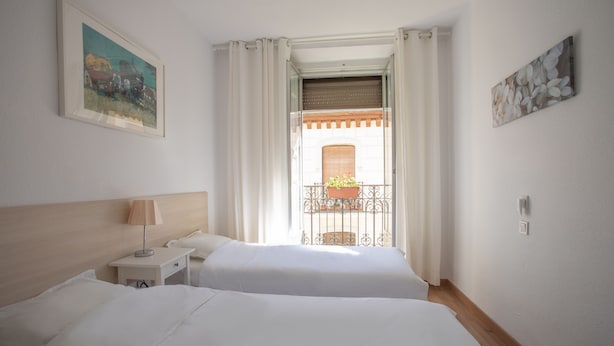 A hotel room with two beds, a nightstand, a lamp, and a view of a balcony with a railing. - nalon inn (Madrid)