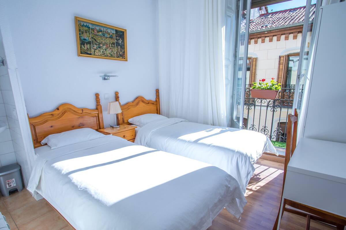 Une chambre d’hôtel avec deux lits, une tête de lit en bois, une table de chevet avec une lampe et une fenêtre avec des rideaux.