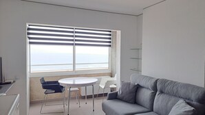 A modern living room with a grey sofa, a small round table, and a TV on a cabinet. - Comfortable flat in EmpuriaBrava by the strand with a stunning view on the bay. (Ampuriabrava)