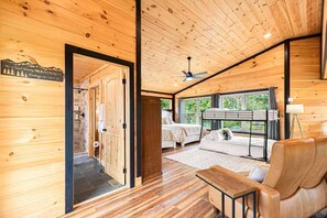L’intérieur d’un chalet en bois, avec un lit, un coin salon et une vue sur l’extérieur.