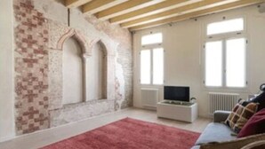 A room with exposed brick walls, a wooden ceiling, a red rug, a white sofa, and a television. - Enchanting flat, in the core of Treviso, the city of Prosecco, pet friendly (Treviso)