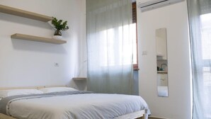 A bedroom with a bed, a plant on a shelf, a mirror, and a window with curtains. - Maison 27 Holiday Home Cremona (CREMONA)