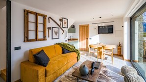 A modern living room with a yellow sofa, a dining area with a wooden table, and a kitchen visible through an open door. - Chalet with sauna H 311 (GORDONA)