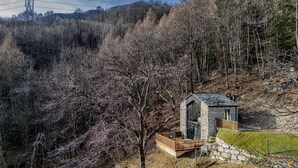 A small stone cabin with a wooden deck, surrounded by trees and a hill in the background. - Chalet with sauna H 311 (GORDONA)