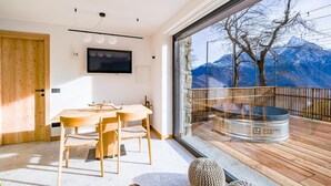 A modern kitchen with a wooden table and chairs, a flat-screen TV mounted on the wall, and a large window overlooking a mountainous landscape. - Chalet with sauna H 311 (GORDONA)
