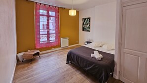 Ein Schlafzimmer mit einem Bett, einem Nachttisch, einem Sessel, einem Heizkörper und einem Fenster mit Vorhängen.