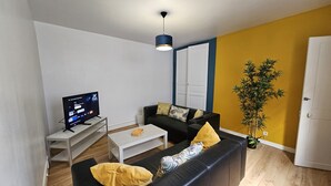 Ein modernes Wohnzimmer mit einer schwarzen Couch, einem Couchtisch, einem Fernseher auf einem Schrank und einer Pflanze.