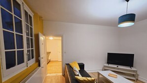Ein Wohnzimmer mit einem schwarzen Sofa, einem Fernseher, einem Holztisch und einer blauen Pendelleuchte.