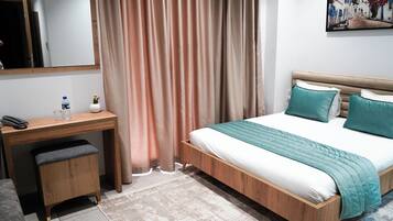 Un dormitorio con cama de madera, escritorio, silla, taburete pequeño, espejo y un cuadro en la pared.