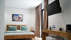 A modern hotel room with a bed, a desk, a television, and a painting on the wall. - Hôtel Suisse (Tunis)